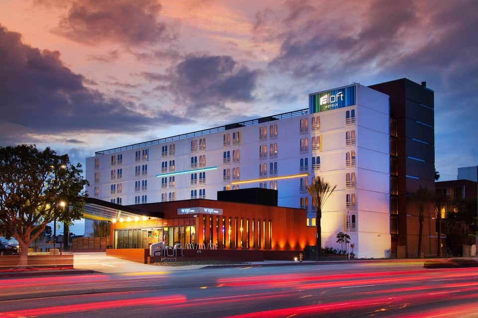 Aloft Hotel exterior at dusk with illuminated white and orange facade against colorful twilight sky