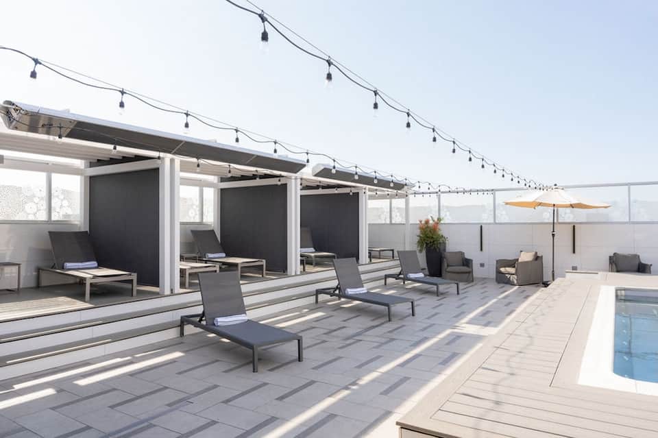 Hotel rooftop lounge with modern cabanas, string lights, lounge chairs, and pool area