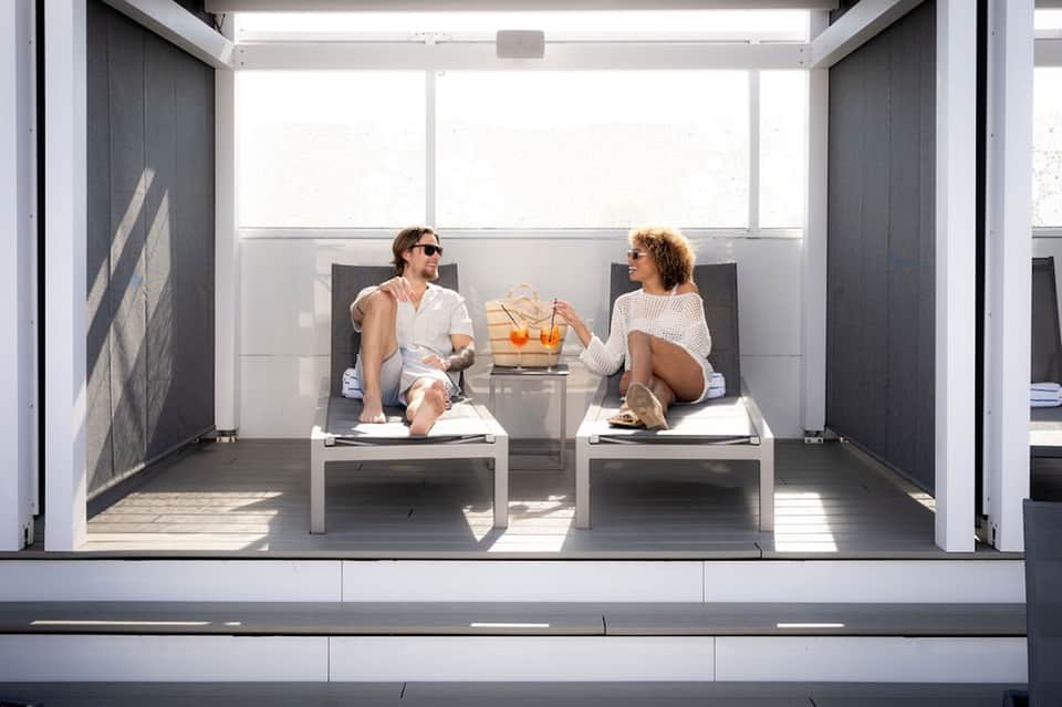 Two guests relaxing on a modern rooftop terrace with white lounge chairs and city views