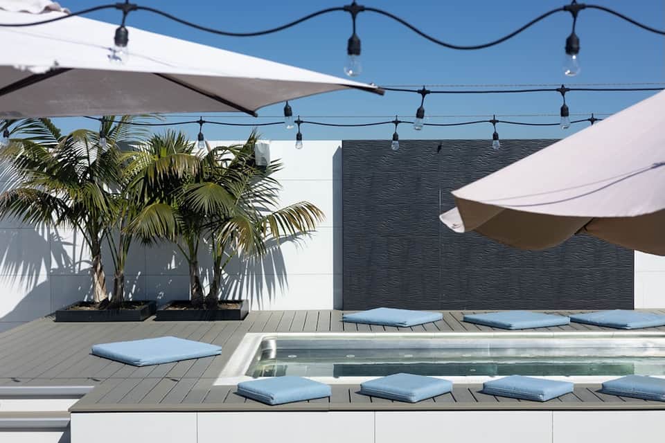 Contemporary rooftop pool deck with loungers, shade sails, and string lighting