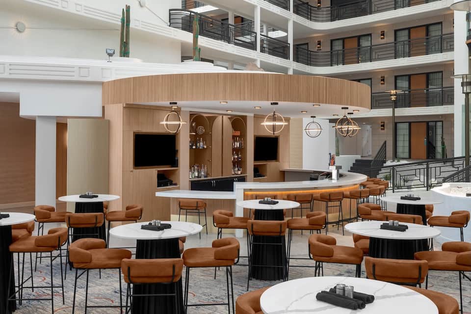 Contemporary hotel bar and lounge with wooden accents, tan leather chairs, and white tables