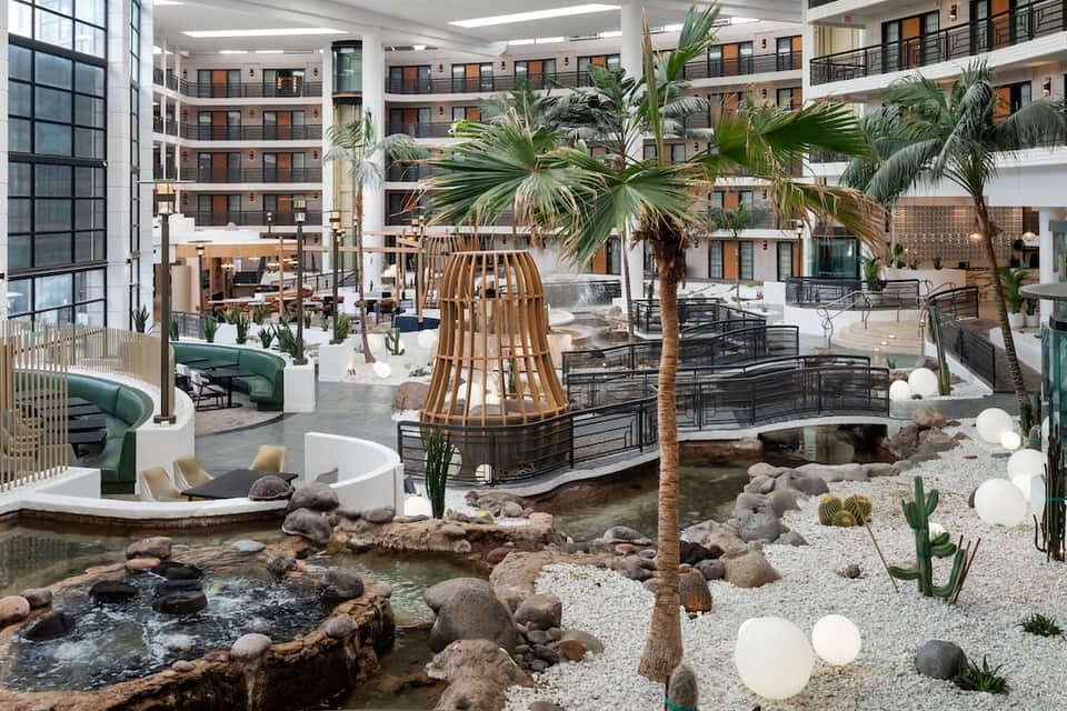 Multi-level hotel atrium with tropical plants, water feature, and surrounding guest room balconies