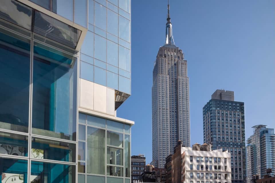 Manhattan street view with modern glass building in foreground and iconic Empire State Building in background.