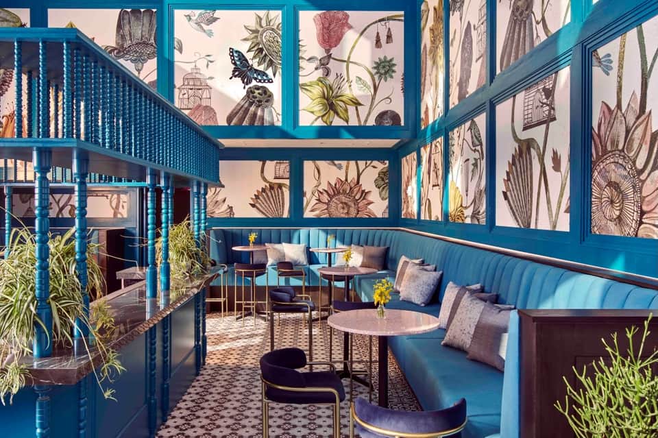 Turquoise lounge with botanical wall art, blue velvet seating, and tiered mezzanine design