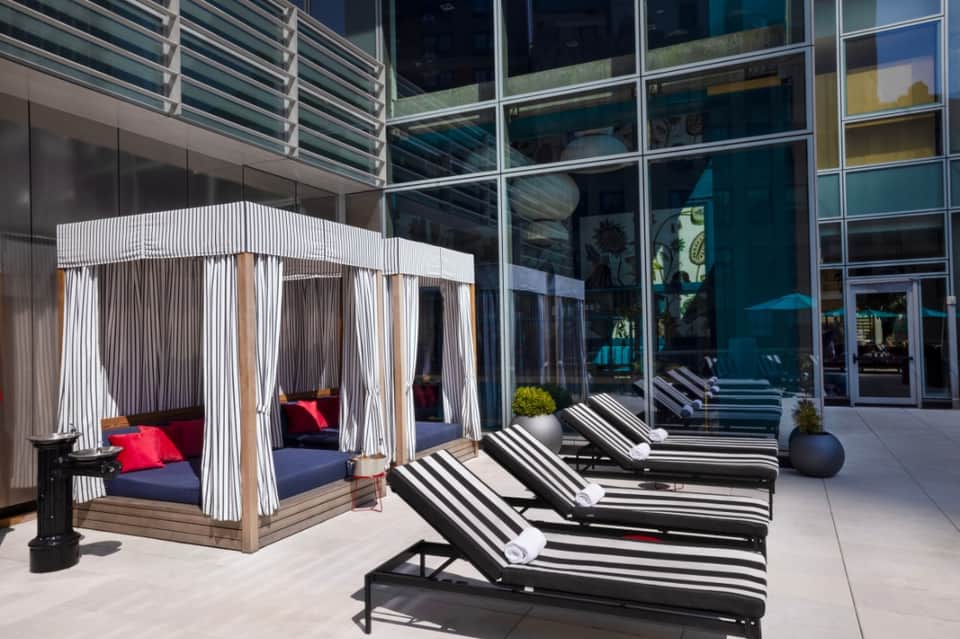 Modern poolside deck with striped lounge chairs and cabana tent with red pillows near building