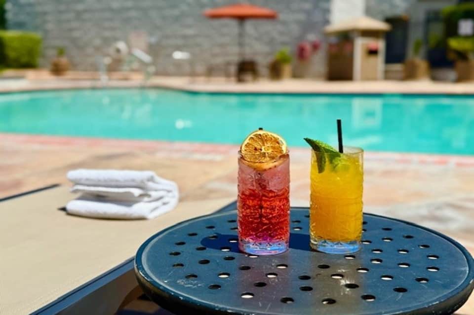 Colorful cocktails on poolside table with resort pool and umbrellas in background