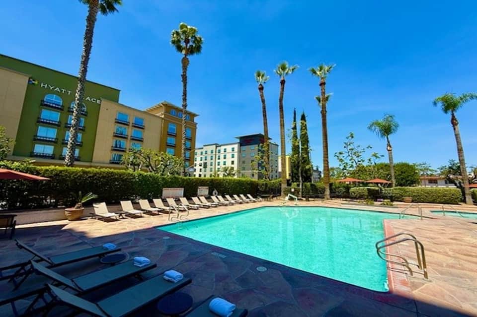 Resort pool deck with turquoise water, palm trees, lounge chairs, and Hyatt Ace hotel building exterior