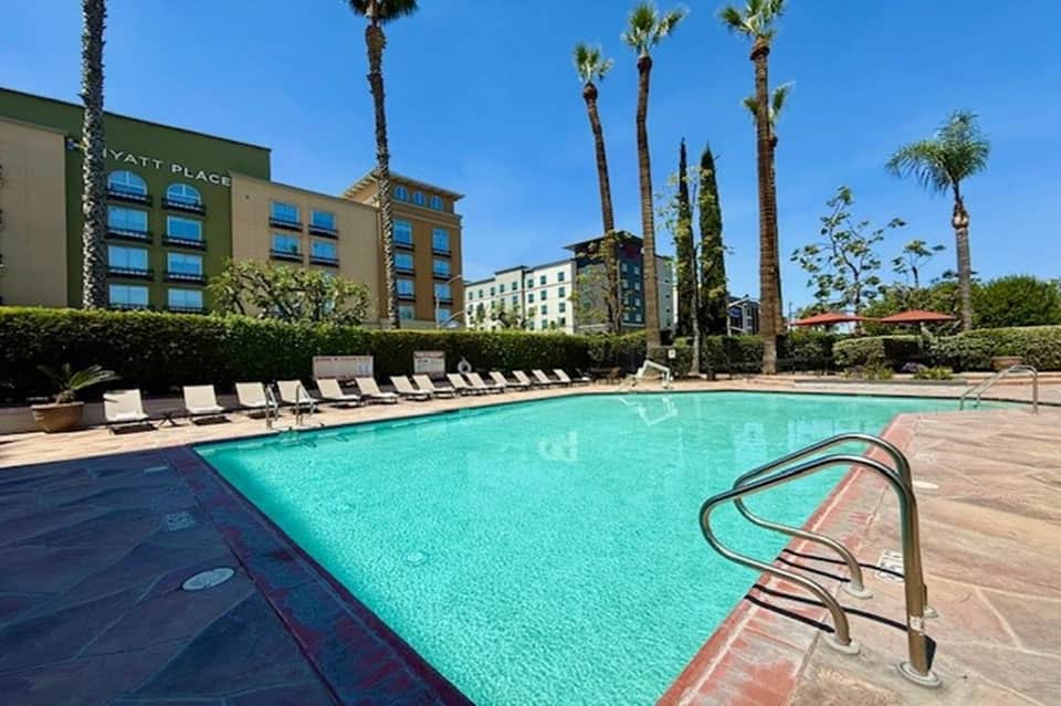 Resort pool with turquoise water, lounge chairs, palm trees, and hotel buildings in background