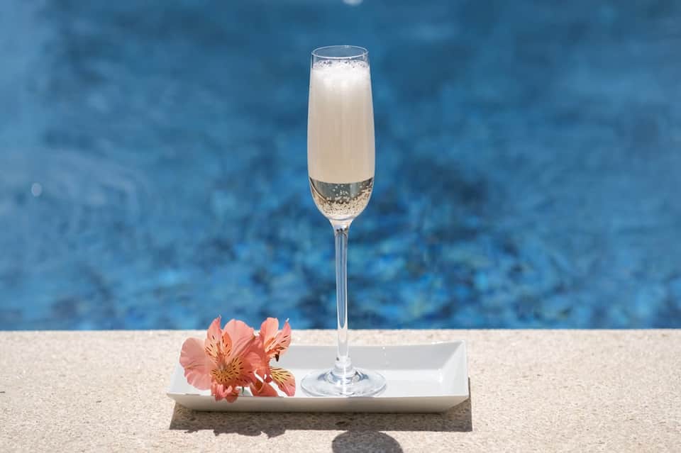Champagne cocktail with coral flower at poolside overlooking blue water