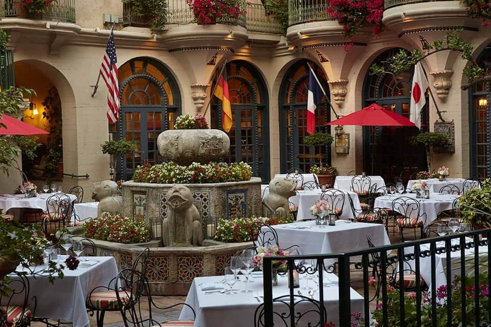 Upscale courtyard dining area with fountain, formal tables, archways, and international flags