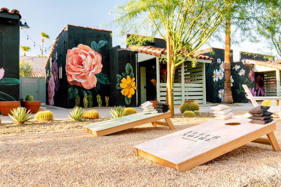Desert resort courtyard with colorful mural walls, cacti, cornhole boards, and palm trees