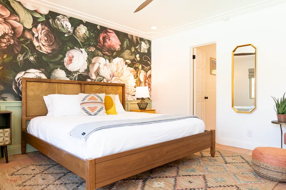 Bedroom with wooden bed frame, floral wallpaper accent, and coastal décor