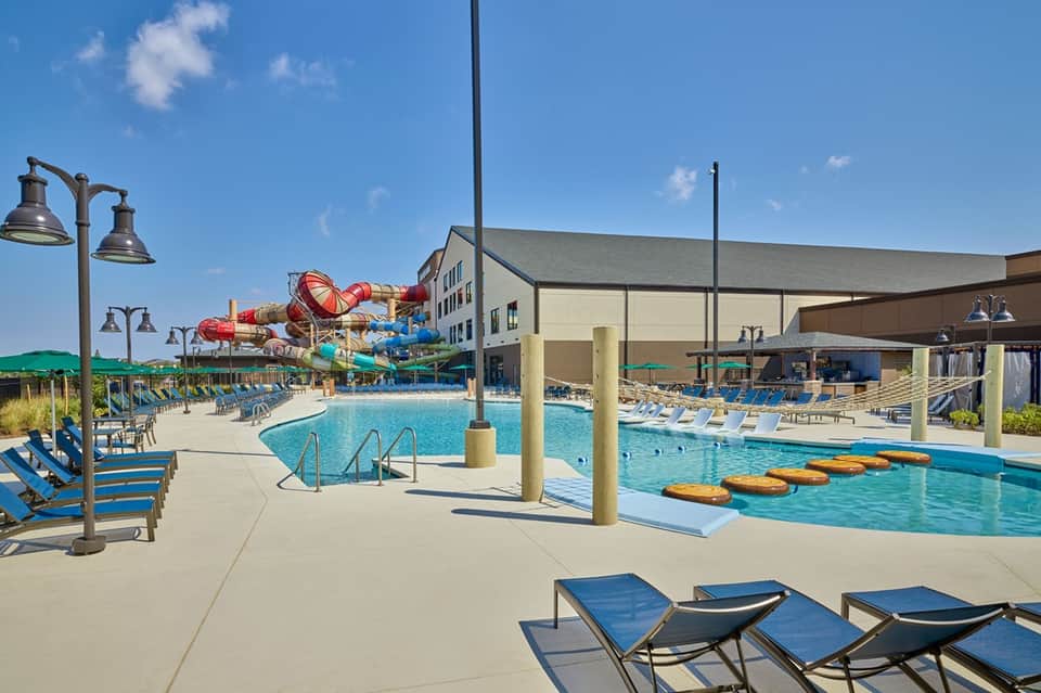 Daytime resort pool with waterslide, multiple pools, and blue lounge chairs