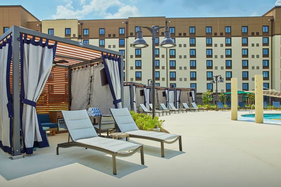 Outdoor resort deck with navy cabanas, lounge chairs, large hotel building, and blue pool water visible