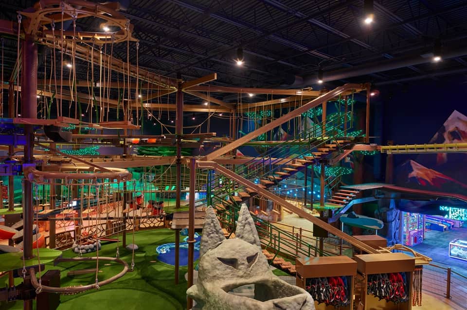 Indoor adventure park with multi-level wooden structures, rope courses, and climbing obstacles