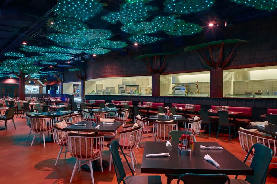 Upscale restaurant with illuminated tree canopy ceiling, red booths, round tables, and modern dining setup