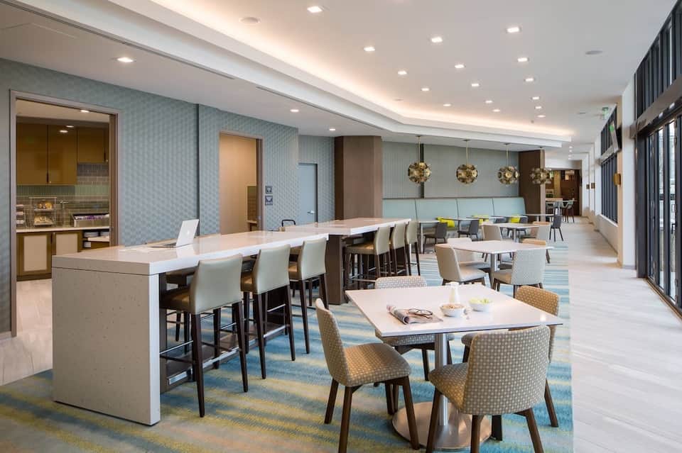 Contemporary hotel common area with bar seating, tables, blue patterned walls, and pendant lighting