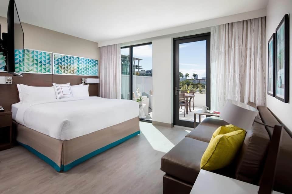 Modern hotel bedroom with king bed, balcony access, ocean view, and contemporary furnishings