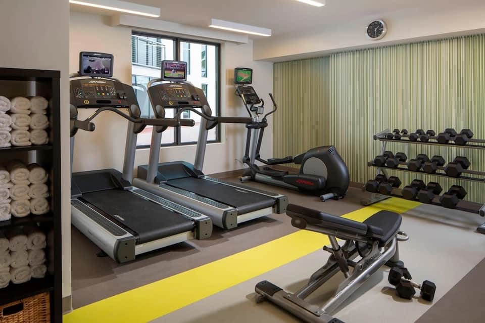 Modern fitness center with treadmills, exercise bikes, dumbbells, and green accent wall
