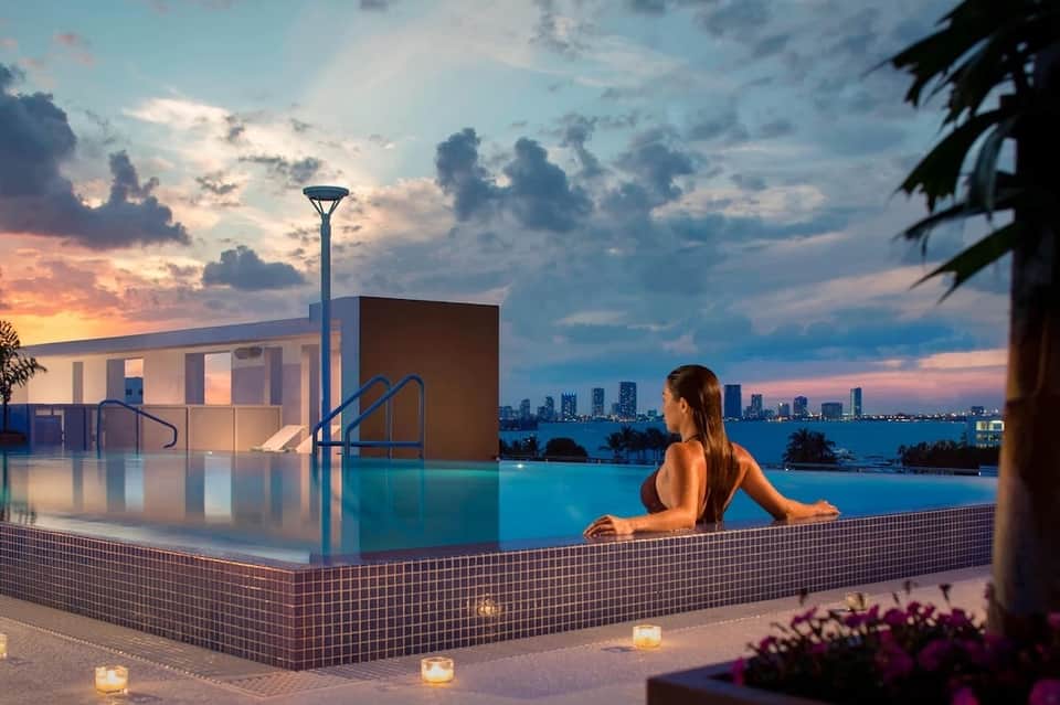 Woman relaxing in infinity pool at sunset with city skyline in background