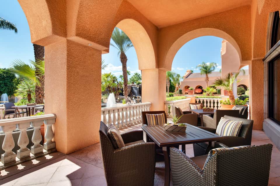 Terracotta-colored Spanish colonial architecture with arched covered patio, wicker seating, and tropical palm gardens