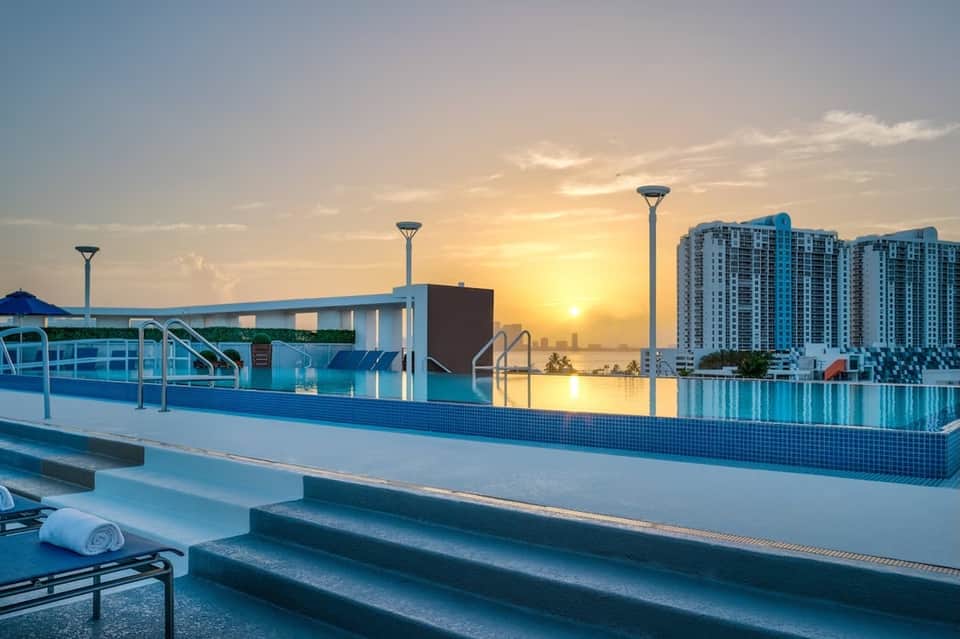 Rooftop infinity pool at sunset with city skyline and high-rise buildings reflected in calm water