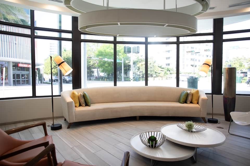 Modern circular lobby lounge with curved cream sofa, floor-to-ceiling windows, and contemporary furnishings
