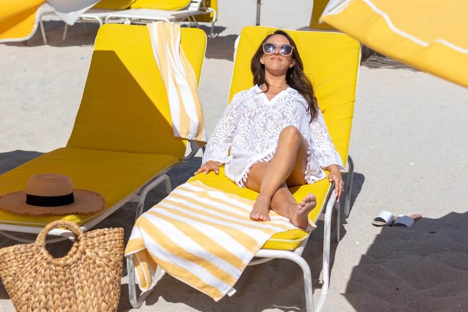 Woman relaxing on yellow beach lounger with striped towel and sunglasses
