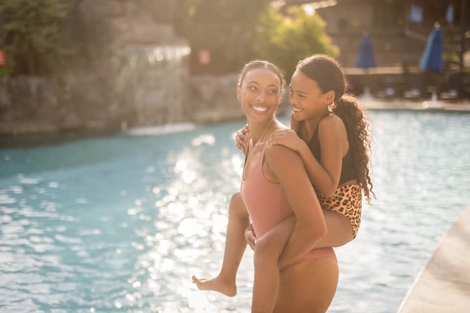 Two young girls smiling by a resort swimming pool on a sunny day