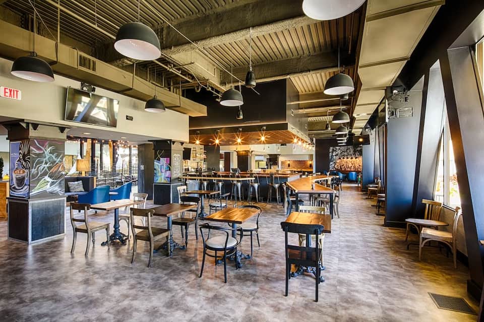 Contemporary restaurant and bar space with wooden tables, industrial ceiling, and blue accents