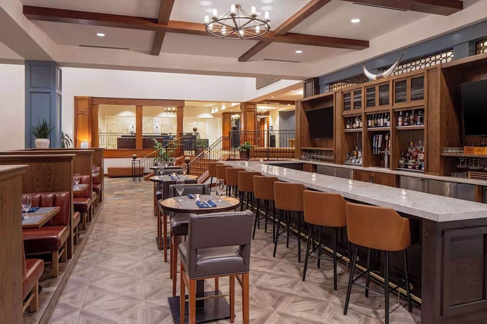 Upscale bar lounge with wood paneling, leather seating, and extensive liquor shelves