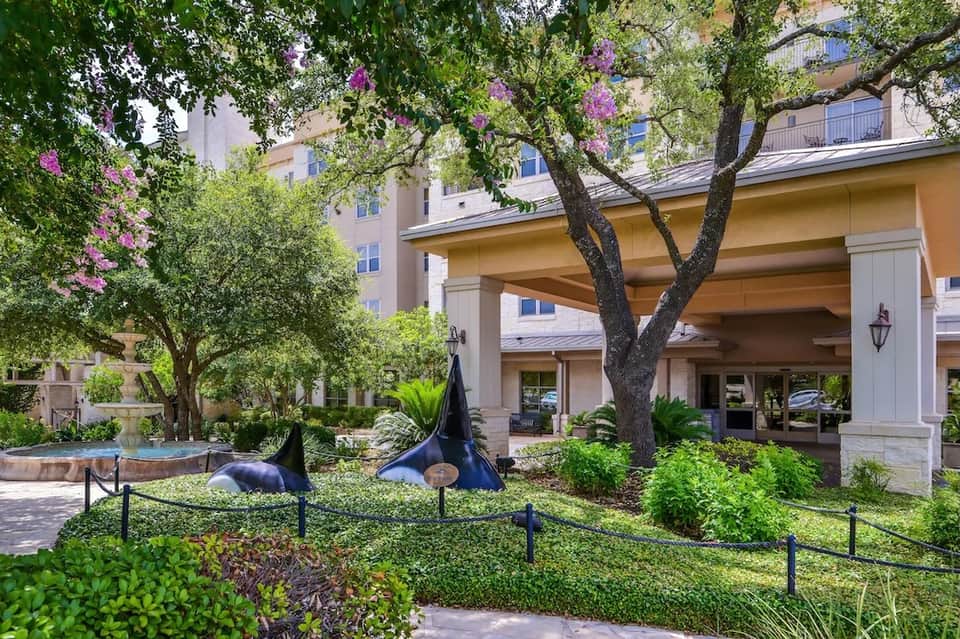 Resort courtyard with whale tail sculptures, lush vegetation, and hotel building