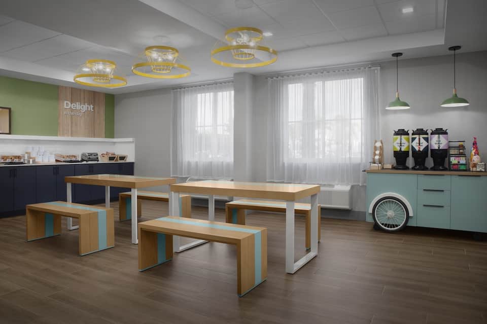Modern cafeteria with wooden tables, white benches, turquoise accents, pendant lights, and large bright windows