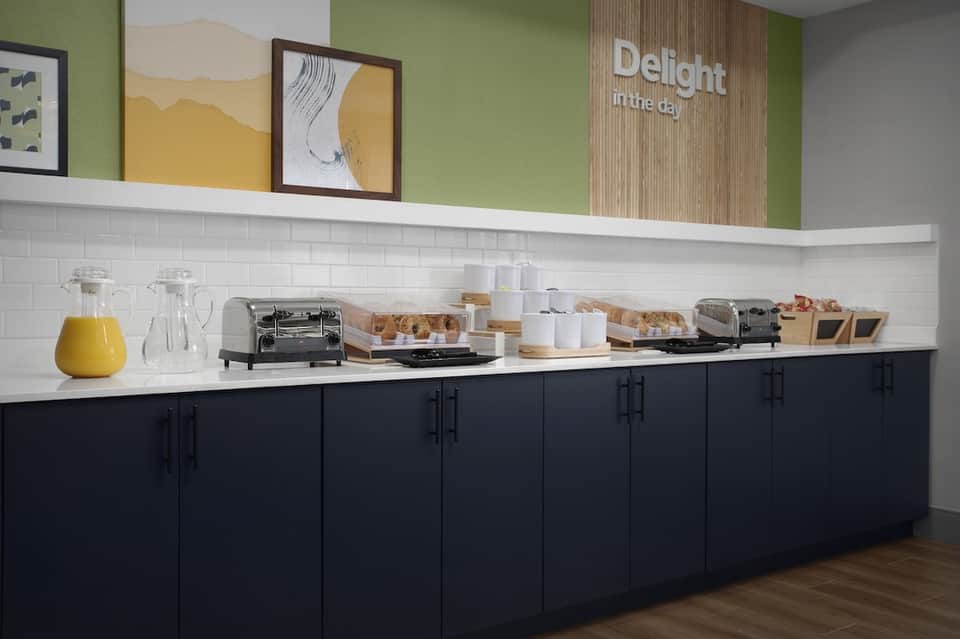 Breakfast buffet station with pastries, juice, and coffee service with green accent wall