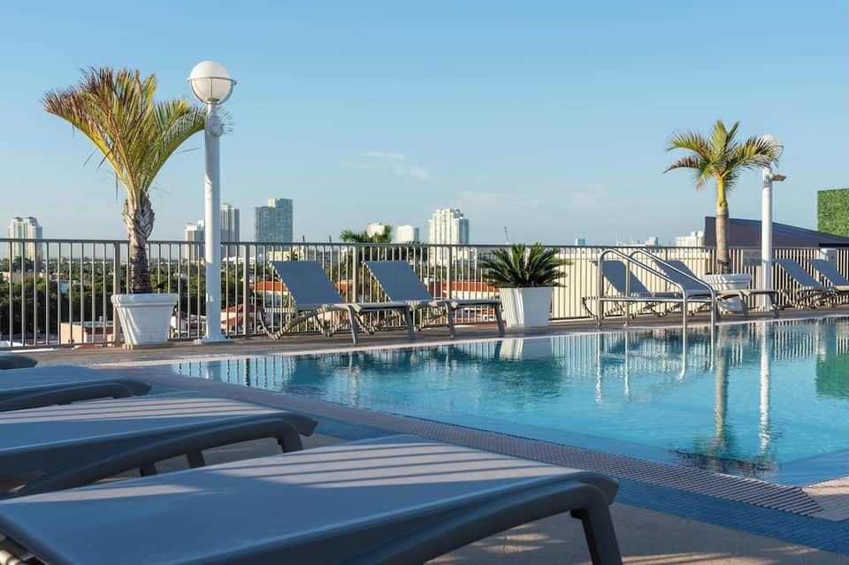 Resort rooftop pool overlooking city skyline with palm trees and lounge chairs
