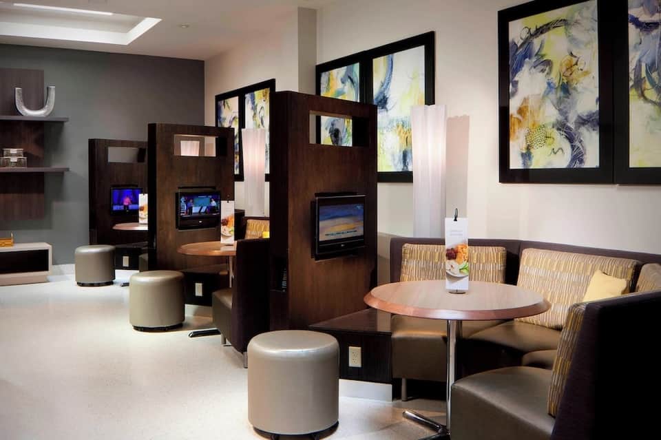 Contemporary hotel lobby lounge with dark wood room dividers, cream seating, and abstract framed artwork