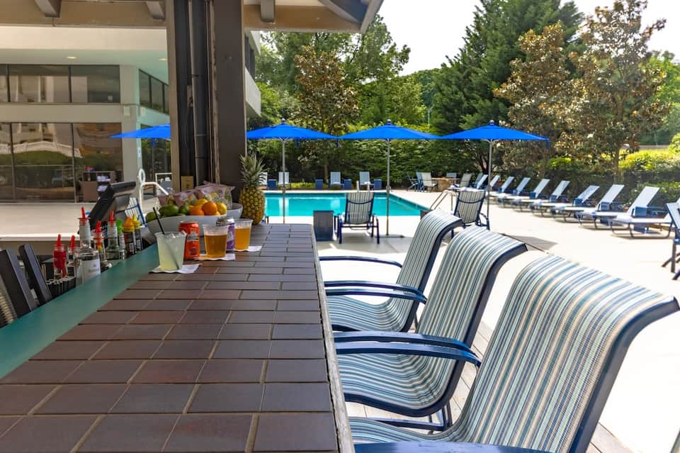 Resort pool deck with blue umbrellas, lounge chairs, and beverage station