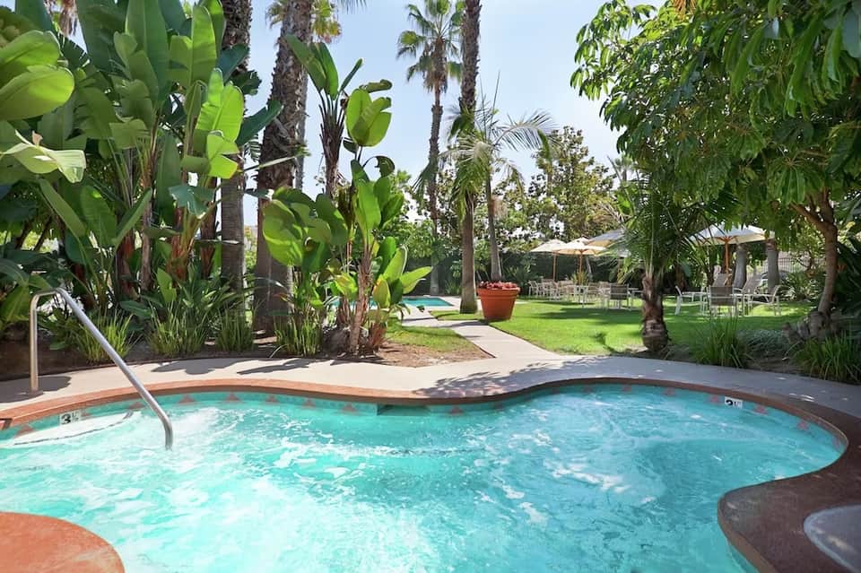 Resort spa pool surrounded by lush tropical vegetation, palm trees, lounge chairs, and poolside cabanas