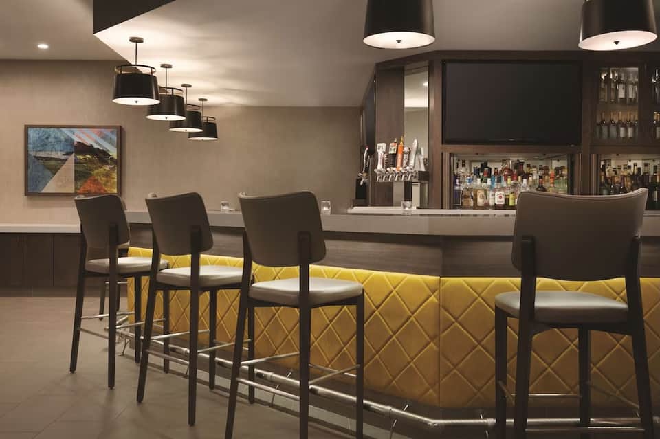 Contemporary lounge bar with yellow quilted seating, black chairs, pendant lights, and full bar