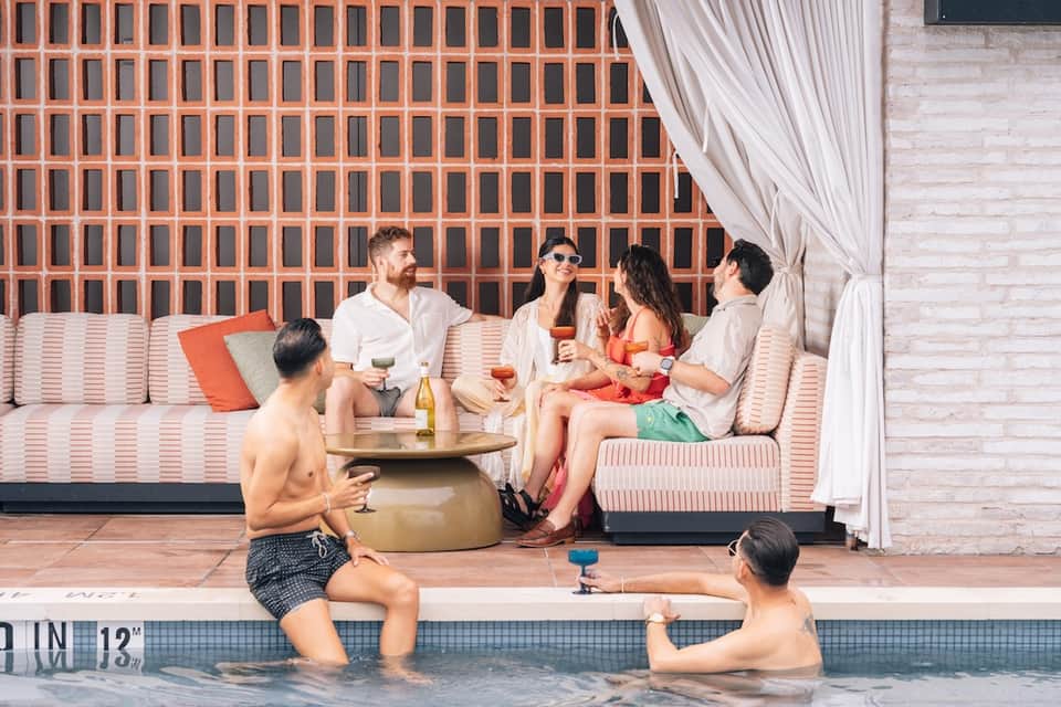 Guests relaxing poolside on loungers and in water near modern resort with striped cushions and white curtains