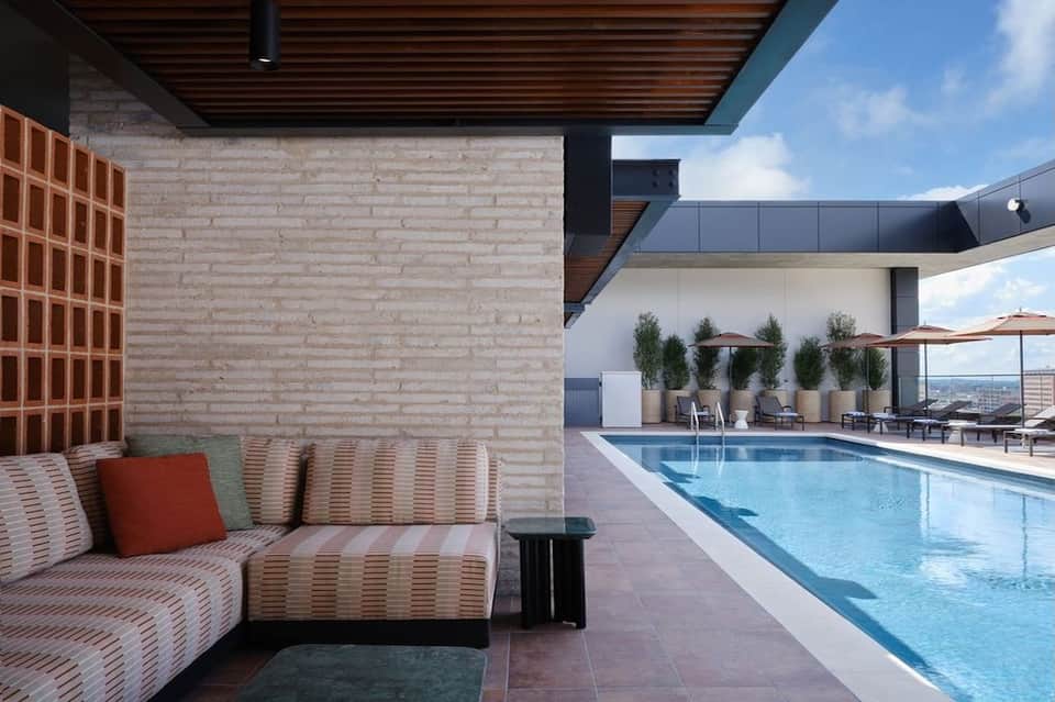 Striped modern seating area beside rectangular pool with white walls, potted plants, and lounge chairs