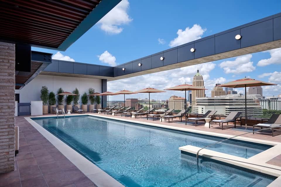 Rooftop pool with lounge chairs, umbrellas and city skyline view
