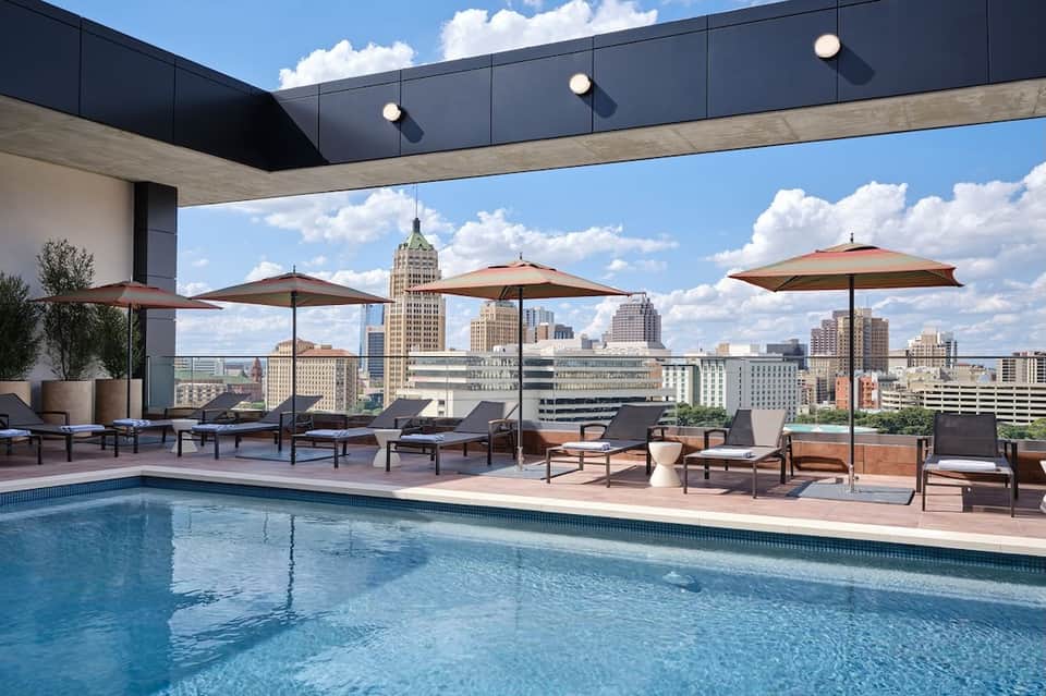 Rooftop pool with city skyline views, lounge chairs, umbrellas, and modern architecture