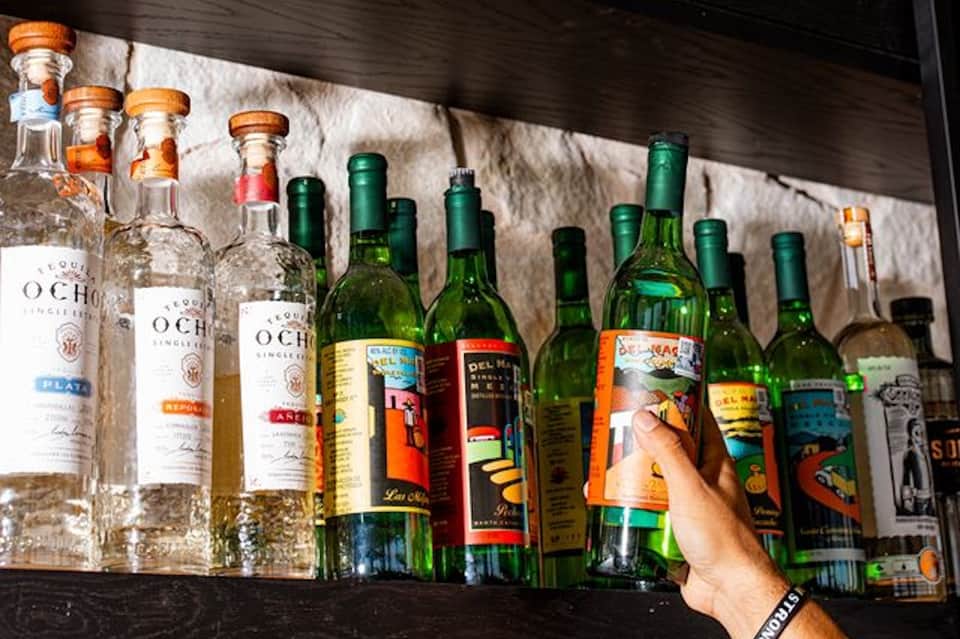 Shelf displaying bottles of tequila and various spirits with wooden beams above