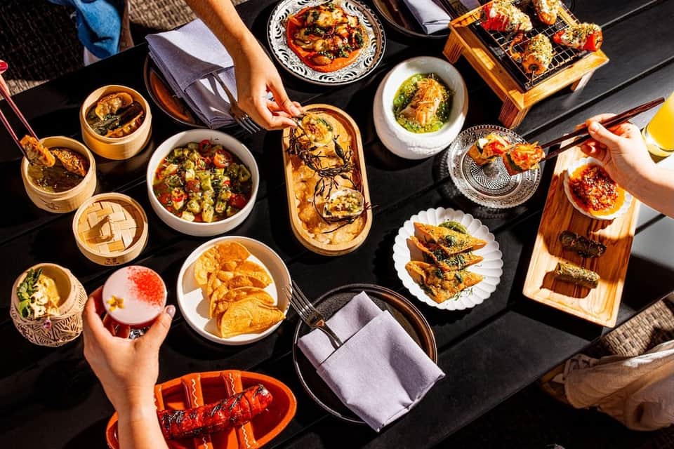 Overhead view of shared dining table with Asian cuisine, dim sum, and grilled items