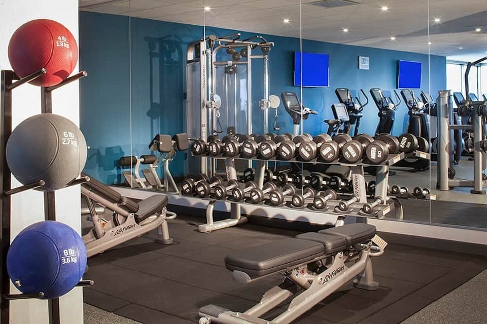 Modern gym with dumbbells, exercise machines, and mirrored walls in bright blue room