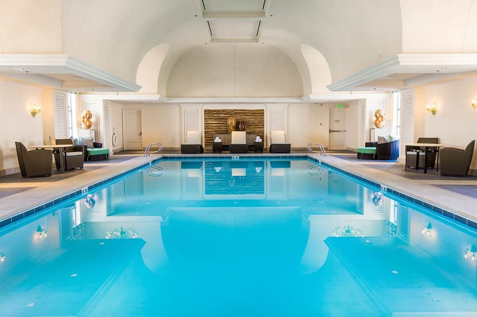 Indoor hotel pool with arched ceiling, blue water, cream-colored architecture, and ambient lighting