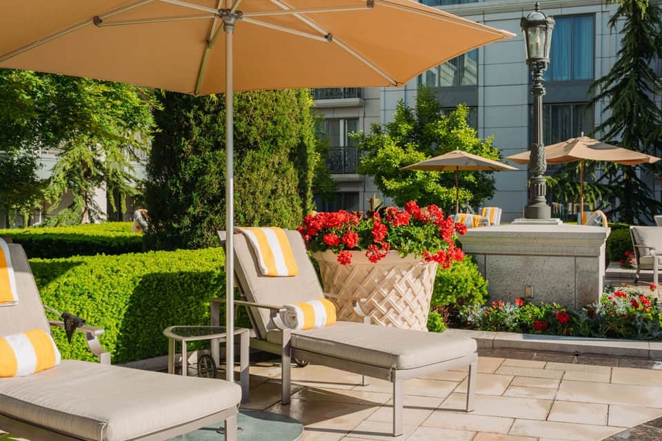 Outdoor garden lounge with tan umbrellas, lounge chairs, and red flowering plants