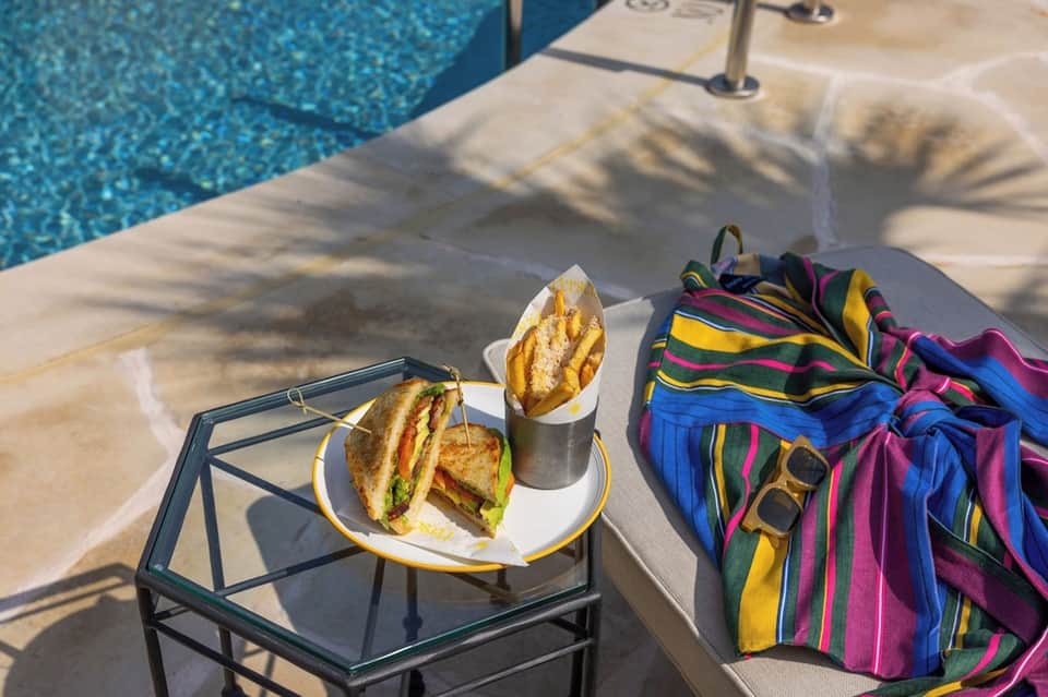 Poolside lunch with sandwich, drink, and colorful striped beach towel