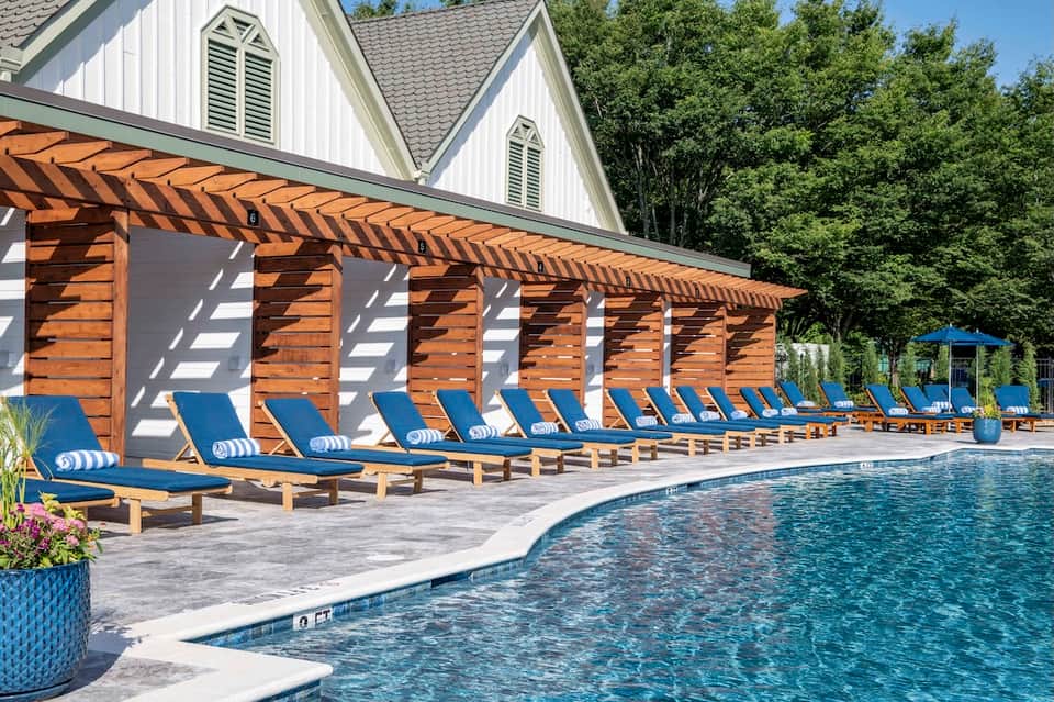Outdoor pool area with modern pergola cabanas, blue lounge chairs, and mature landscaping